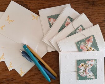 May include: White stationery set with butterfly accents. Includes envelopes with yellow butterfly corner designs, and cards with floral butterfly embellishments. Three pens in blue and yellow are also present.