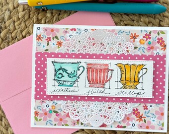 May include: A handmade greeting card with a pink polka dot border and floral accents. The card features three teacup illustrations labeled "icanthus", "fluted", and "scallop". Three pens in pink, yellow, and teal are on top of the card.