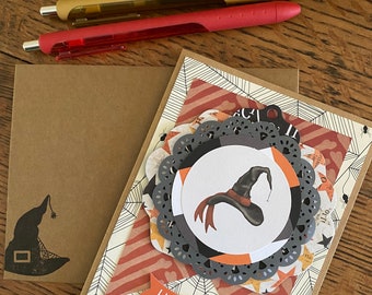 May include: A handmade Halloween card with a witch's hat and the text "Happy Halloween". The card is decorated with orange, red, and black paper and has a lace-like design.