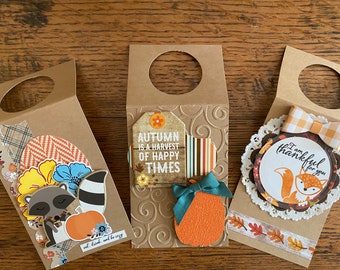 May include: Three brown paper gift bags with cut-out handles. The bags are decorated with fall-themed embellishments, including a raccoon with a pumpkin, a pumpkin with a green bow, and a fox with a bow and the text "I am thankful for you".