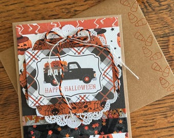 May include: A handmade Halloween card with a black truck carrying pumpkins and a banner that says "BOO". The card has a plaid background and the words "Happy Halloween" are printed on the front.