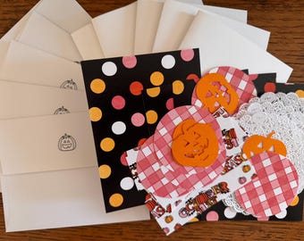 May include: A collection of Halloween-themed stationery. Includes cream-colored envelopes with pumpkin stamps, black cards with polka dots, and decorative cutouts of pumpkins and gingham patterns. Also includes white doilies.
