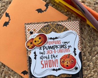 May include: A handmade Halloween greeting card featuring a die-cut label with the text PUMPKINS come & PUMPKINS go, but JACK-O-LANTERNS steal the SHOW! Decorated with pumpkin illustrations, a star, and bats, paired with an orange envelope and four pens.