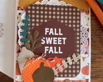 May include: A handmade fall-themed greeting card with the text "FALL SWEET FALL." The card features a brown gingham pattern, decorative pumpkins, and fall foliage. The card is decorated with lace and other embellishments.