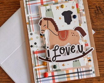 May include: A handmade card with a plaid background and a rocking horse illustration. The card has a white envelope and says "i love u" in a white banner.