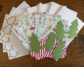 May include: A collection of stationery items including white envelopes with gold outline Christmas tree designs, rectangular cards featuring a light blue background with colorful holiday ornaments, and several die-cut green paper Christmas trees.