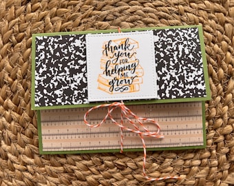 May include: A handmade card with a green border, featuring a black and white composition notebook pattern and a ruler design. The card is tied with red and white twine and has the text "thank you for helping me grow" on a white square.