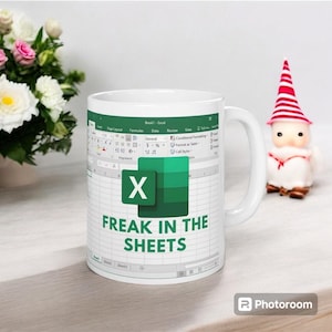 Puede incluir: Taza de cerámica blanca con un diseño de hoja de cálculo de Excel, el logotipo de Microsoft Excel y la frase "FREAK IN THE SHEETS". La taza tiene un asa blanca y está diseñada para bebidas frías o calientes.
