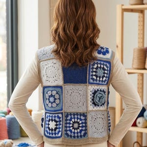 Puede incluir: Un chaleco sin mangas confeccionado con un mosaico de cuadrados de ganchillo en varios tonos de azul, blanco y gris. La prenda presenta intrincados patrones florales y geométricos dentro de cada cuadrado, unidos por un borde de hilo color canela.