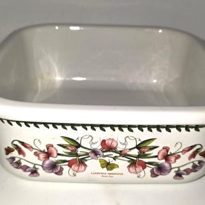 May include: A white square ceramic baking dish featuring a botanical illustration of pink and purple sweet pea flowers with green vines and a small yellow butterfly. The text LATHYRUS ODORATUS Sweet Pea is printed below the floral design.