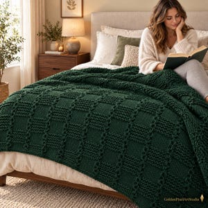 May include: A dark forest green chunky knit throw blanket featuring a textured basketweave pattern. The blanket is draped over a bed, showcasing thick yarn stitches and a consistent square grid design throughout the fabric, providing a heavy, warm appearance.