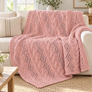 Può includere: Una coperta lavorata a maglia color rosa antico con un motivo testurizzato di trecce diagonali alternate a sezioni traforate a forma di diamante. La coperta presenta un bordo spesso e a coste con una lavorazione a maglia grossa.