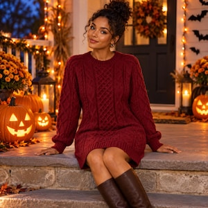 May include: A deep red cable knit sweater dress featuring a crew neckline, long sleeves with ribbed cuffs, and a textured pattern of vertical cables and diamond shapes throughout the garment, paired with dark brown knee-high leather boots.