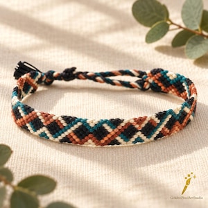 May include: A woven friendship bracelet featuring a repeating geometric diamond pattern in black, cream, teal, and rust orange thread. The bracelet is constructed from multiple strands of cord with a braided tie closure at the end.