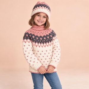 May include: A cream-colored knit sweater and matching beanie featuring a pink and dark gray geometric pattern. The sweater has a high turtleneck collar, long sleeves, and a ribbed hem. The beanie has a ribbed cuff and a small pom-pom on top.
