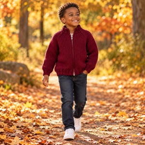 May include: A deep burgundy, chunky knit zip-up sweater with a ribbed collar and cuffs, paired with dark blue denim jeans and white sneakers. The sweater features a full-length silver zipper closure and a thick, textured knit pattern throughout.