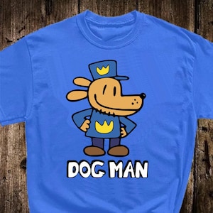 May include: A blue t-shirt featuring a cartoon dog character in a police uniform with a yellow crown on the hat and chest. The text "DOG MAN" is printed in white block letters below the character.