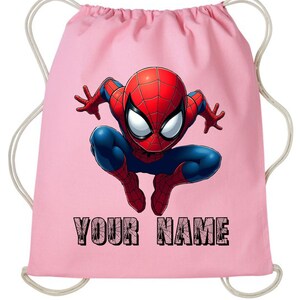 May include: A pink drawstring bag featuring a colorful illustration of Spider-Man in a crouching pose. The superhero is depicted in his classic red and blue suit. The text "YOUR NAME" is printed in black at the bottom.