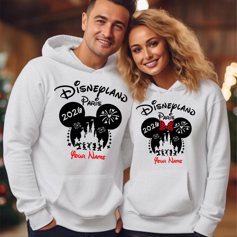 Może przedstawiać: Białe bluzy z kapturem z nadrukiem Disneyland Paris 2020. Projekt zawiera uszy Myszki Miki, fajerwerki i sylwetkę zamku. Tekst "Your Name" znajduje się poniżej.