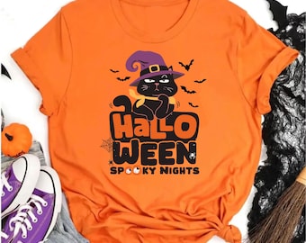 Pode incluir: Uma t-shirt laranja de manga curta com o gráfico de um gato preto a usar um chapéu de bruxa roxo e um cachecol amarelo. O texto diz HALLOWEEN SPOOKY NIGHTS, acompanhado por ilustrações de morcegos, uma teia de aranha e uma pequena aranha.