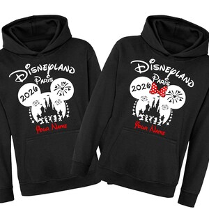 Może przedstawiać: Czarne bluzy z kapturem z logo Disneyland Paris, uszami Myszki Miki i rokiem 2020. Jedna bluza ma czerwoną kokardę. Tekst "Your Name" jest wydrukowany na czerwono pod projektem.