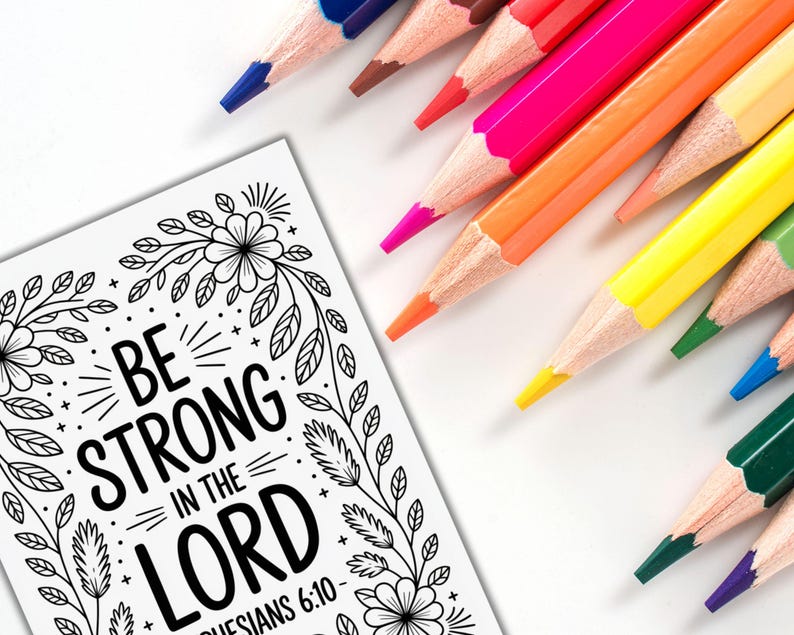 May include: A coloring page with the text "BE STRONG IN THE LORD" and floral border is next to a collection of sharpened colored pencils in various colors. The pencils are arranged diagonally across a white surface, ready for use.