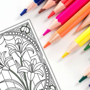 May include: A coloring page featuring a floral design with lilies, alongside a collection of colored pencils in various shades. The pencils are arranged diagonally, with colors including blue, red, pink, orange, yellow, and green. The image is set against a white background.