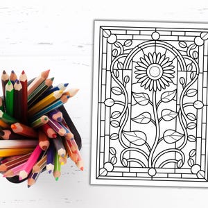 May include: A black container filled with a variety of colored pencils next to a black and white line drawing of a sunflower. The sunflower drawing is in a stained glass style with a floral design.