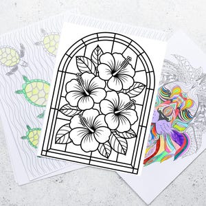 May include: Three coloring book pages. One features a black and white hibiscus flower design, another has a lion with colorful details, and the third shows turtles swimming in the ocean. The pages are on a light gray surface.