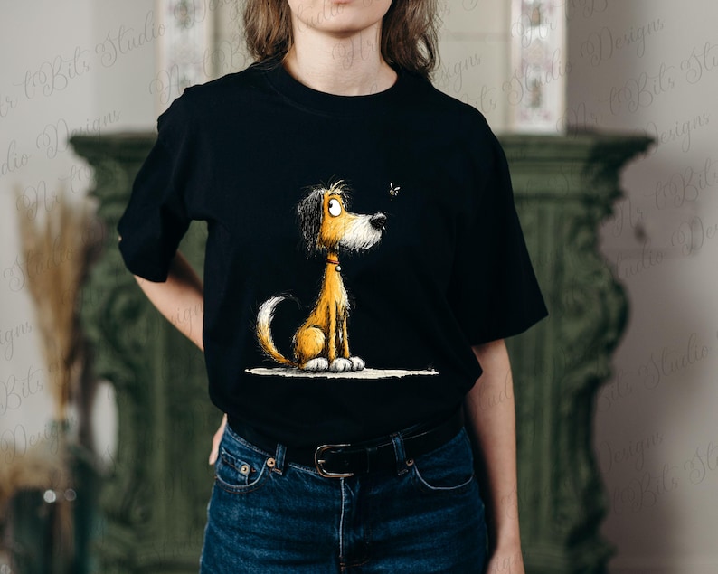 May include: Black t-shirt featuring a cartoon dog with brown and yellow fur, sitting and looking at a small insect. The dog has a white tail and paws, and a red collar. The graphic is centered on the shirt.