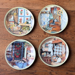 May include: Four round decorative ceramic plates featuring detailed illustrations of cats in various indoor and outdoor settings. Each plate has a yellow and white checkered border and depicts scenes with furniture, plants, quilts, and multiple cats.