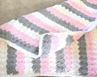 Manta de bebé tejida a crochet gruesa, hecha a mano, con rayas rosas, grises y blancas.
