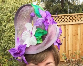 Amethyst Twist hat in shimmering lavendar sinamay headpiece with handmade orchids and hibiscus flowers, handsewn silk bias brim.  In Stock