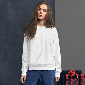 May include: A white crew neck sweatshirt featuring the gold text "Timing Always". The sweatshirt is worn with blue jeans. The design is simple and the outfit has a relaxed, everyday feel.
