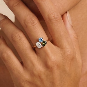 May include: A gold ring with a cluster of gemstones. The ring features a light blue, white, and green gemstone design. The ring is worn on a finger.