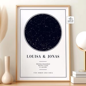 Könnte beinhalten: Ein gerahmter Druck mit einer dunkelblauen Himmelskarte in einem kreisförmigen Design. Die Namen "LOUISA & JONAS" sind über der Stadt, dem Datum und den Koordinaten aufgedruckt. Der Text "FÜR IMMER UND EWIG" ist unten aufgedruckt. Der Rahmen ist hellbraun.