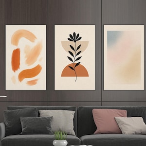 Op de afbeelding: Een moderne woonkamer met een donkergrijze bank, een grijze fauteuil en een witte marmeren salontafel. Drie abstracte kunstprints hangen boven de bank. Een blauw en grijs tapijt bedekt de vloer.