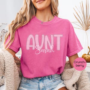 May include: Aunt Sarah t-shirt in a vibrant pink hue. The word "AUNT" is in a gingham pattern, with "Sarah" in a cursive font. The shirt is a comfortable, casual style, perfect for everyday wear.