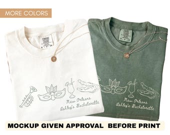 May include: Two t-shirts, one white and one green, with a New Orleans-themed design. The design includes a trumpet, mask, cocktail, and alligator. The text "New Orleans Ashley's Bachelorette" is printed on the shirts. Each shirt has a gold necklace.