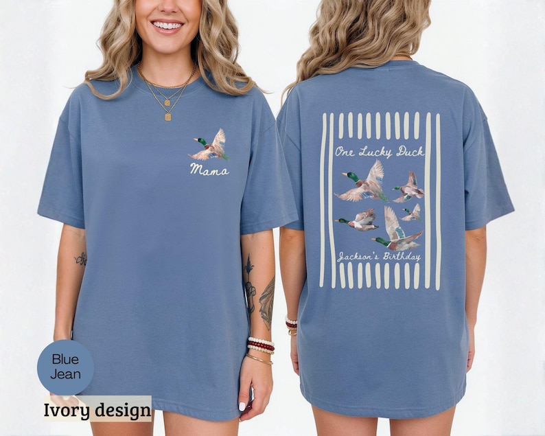 May include: Blue jean colored t-shirt with a duck graphic. The front of the shirt has the word "Mama" and a duck graphic. The back of the shirt has the text "One Lucky Duck" and "Jackson's Birthday" with a duck graphic.