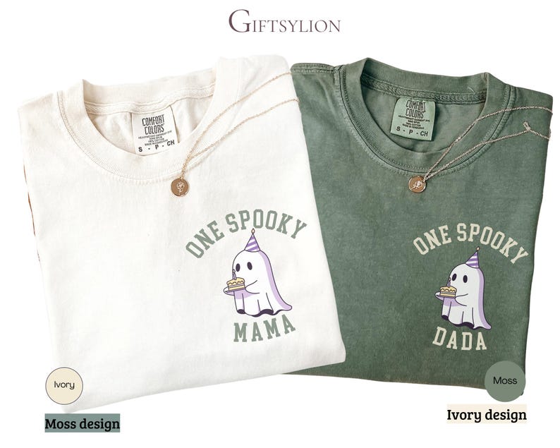May include: An ivory and a moss green t-shirt, each featuring a graphic of a ghost wearing a purple striped party hat and holding a birthday cake. The ivory shirt has the text ONE SPOOKY MAMA, and the moss green shirt has the text ONE SPOOKY DADA.