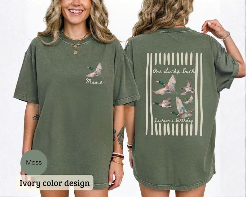 May include: Moss green t-shirt with a duck graphic. The front of the shirt has a duck graphic and the word "Mama". The back of the shirt has a rectangular design with the words "One Lucky Duck" and "Jackson's Birthday" with duck graphics.