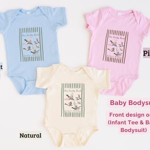 May include: Baby bodysuits in light blue, pink, and natural colors. Each bodysuit features a rectangular graphic with the text "One Lucky Duck" and a watercolor illustration of ducks in flight. The design is on the front only.
