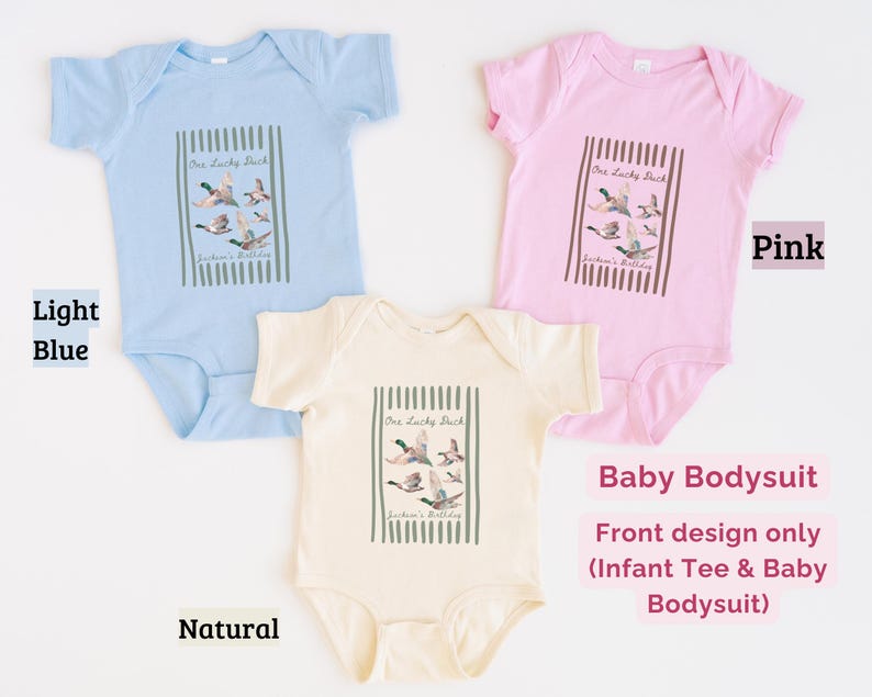 May include: Baby bodysuits in light blue, pink, and natural colors. Each bodysuit features a rectangular graphic with the text "One Lucky Duck" and a watercolor illustration of ducks in flight. The design is on the front only.