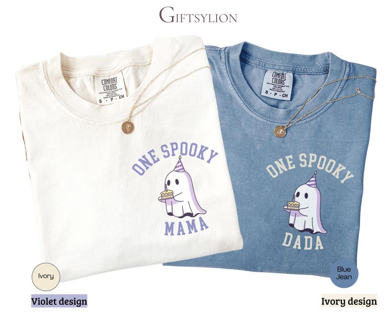 May include: Two short-sleeve crew neck t-shirts, one ivory and one blue jean, each featuring a graphic of a ghost wearing a party hat and holding a birthday cake. The ivory shirt has violet text reading ONE SPOOKY MAMA, while the blue shirt has ivory text reading ONE SPOOKY DADA.