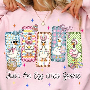 May include: Pink sweatshirt with a graphic of cartoon geese dressed for Easter. Each goose is in a colorful frame, holding Easter eggs or wearing bunny ears. The text "Just An Egg-Cited Goose" is below the graphic.