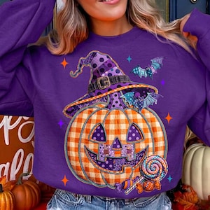 May include: A purple long-sleeve sweatshirt featuring a graphic of a jack-o'-lantern wearing a polka-dot witch hat. The pumpkin has an orange and white gingham pattern, and the design includes two small bats, a lollipop, and colorful stars.