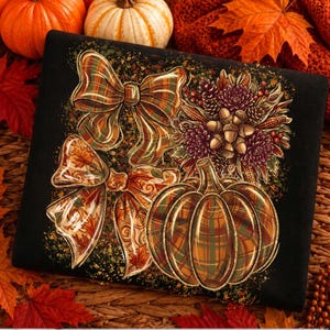 May include: A black fabric item featuring a printed design of two decorative bows, a pumpkin with a plaid pattern, and a cluster of autumn elements including acorns, pinecones, and flowers in shades of orange, brown, green, and deep red.
