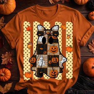 May include: An orange t-shirt featuring a central graphic of a ghost wearing a bow, set against vertical stripes with polka dots. The ghost design incorporates a plaid pattern, small pumpkins, and additional ghost figures in a seasonal theme.