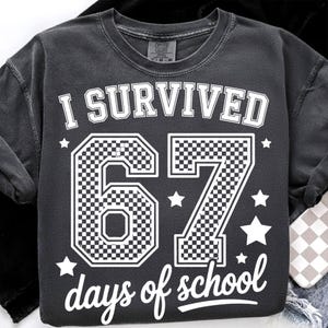 May include: Dark gray sweatshirt with the text "I SURVIVED 67 days of school" in white. The numbers 6 and 7 have a checkered pattern. White stars are scattered around the text and numbers.